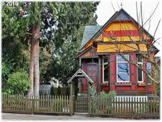 a red and yellow house sitting next to a tree in front of a wooden fence