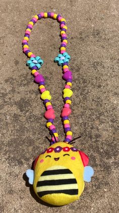 a yellow stuffed animal with colorful beads on it's neck and eyes is laying on the ground