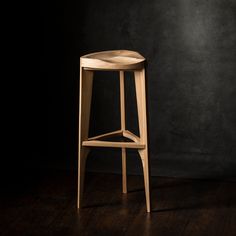 a wooden stool sitting on top of a hard wood floor next to a black wall