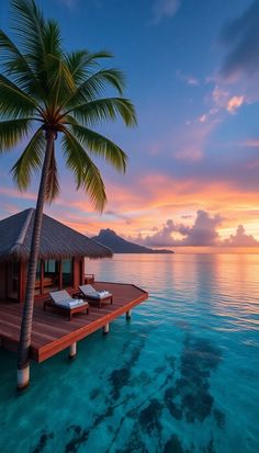 the sun is setting on an island with two chaise lounges and a palm tree