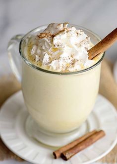 a glass cup filled with whipped cream and cinnamon sticks on top of a white plate