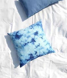 two blue pillows sitting on top of a bed next to white sheets and pillow cases