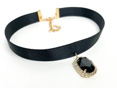 a black choker with a gold chain and a pendant on the side, sitting on a white surface