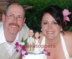 a man and woman pose for a photo in front of a cake with figurines on it