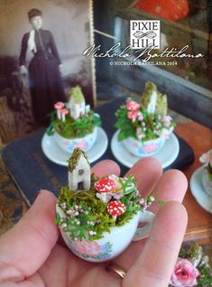 miniature teacups with tiny houses and flowers on them in front of a photo