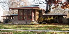 a small brick house sitting in the middle of a leaf covered yard with trees and grass