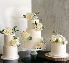 three tiered wedding cakes with white flowers and greenery on the top, sitting on a table