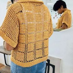 a person standing in front of a mirror wearing a yellow crocheted sweater and jeans