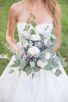 a woman in a wedding dress holding a bridal bouquet with white and blue flowers