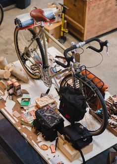 a bicycle parked on top of a wooden table next to bags and other items in front of it