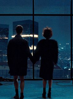 two people standing in front of a window looking out at the city lights and skyscrapers