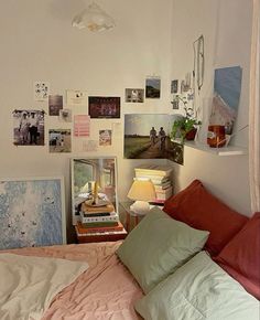 an unmade bed with many pictures on the wall above it and a lamp hanging from the ceiling