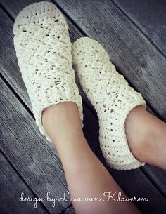 a woman's feet wearing crocheted slippers on top of a wooden floor