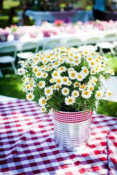 a bunch of daisies in a tin can on a table with checkered cloth