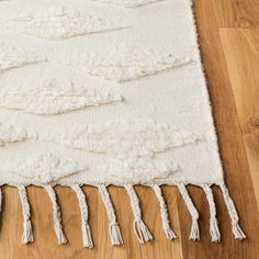 a white rug with tassels on top of it sitting on a wooden floor