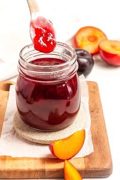 a jar filled with fruit jam on top of a cutting board next to sliced plums