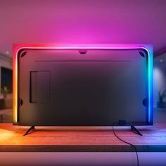 a flat screen tv sitting on top of a wooden table next to a neon light