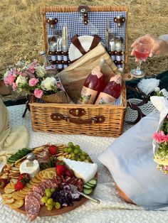 a picnic with wine, cheese and meats in a basket on the ground next to a woman holding a glass of wine