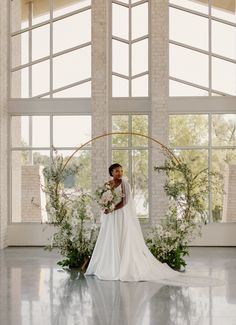 a woman in a wedding dress standing next to an arch with flowers and greenery