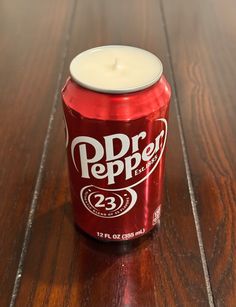 a can of soda sitting on top of a wooden table next to a lit candle