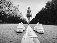 a woman walking down the road between two tennis shoes