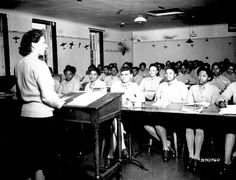 an old black and white photo of women sitting at desks in front of a classroom