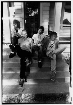 black and white photograph of four people sitting on the front steps of a house with their legs in the air