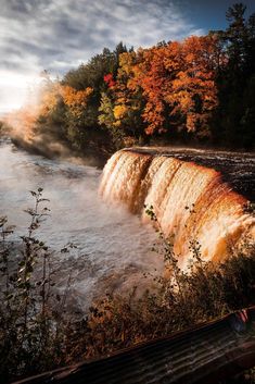 a large waterfall in the middle of a river surrounded by trees with fall colors on it