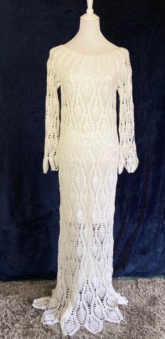 a white crochet dress on a mannequin head stand in front of a blue velvet background