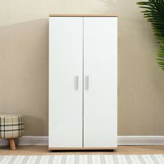 a tall white cabinet next to a plant in a room with a rug on the floor