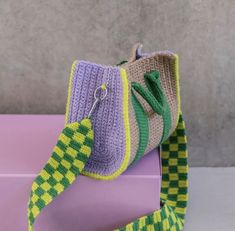 a crocheted purse sitting on top of a purple mat with a green and yellow handle