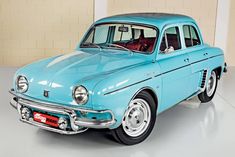 an old blue car is parked in a room with white walls and tile flooring