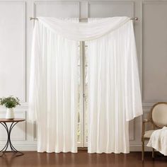 a white drape curtain in a living room next to a table with a chair