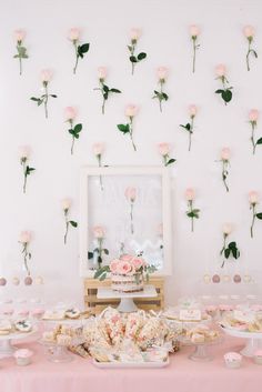 a table topped with lots of desserts and pink flowers on the wall behind it