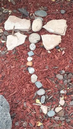 rocks arranged in the shape of a cross on top of red mulch next to a rock