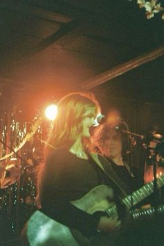 two people on stage playing guitars and singing into microphones with lights in the background