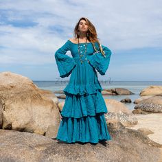 a woman standing on top of a large rock next to the ocean wearing a blue dress