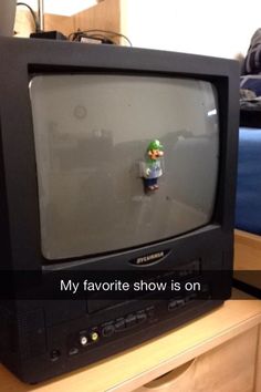 an old tv sitting on top of a wooden dresser next to a small toy figure