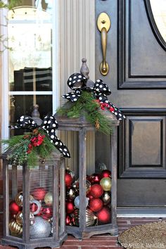 two lanterns with christmas decorations on them sitting outside the front door, decorated for christmas