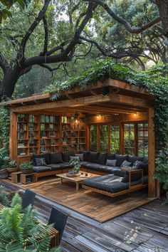 an outdoor living area with couches, tables and bookshelves in the woods