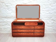 a wooden dresser with a mirror on the top and drawers below it in front of a white brick wall