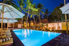 an outdoor swimming pool with lounge chairs and umbrellas around it at night, surrounded by palm trees