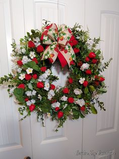 a wreath with red and white flowers hanging on a door