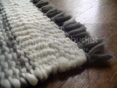 a close up of a rug on a wooden floor with white and gray yarns