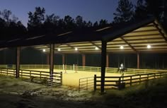 an empty horse barn at night with lights on the stalls and horses in the pen