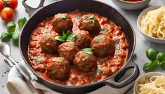 meatballs in tomato sauce with pasta, tomatoes and basil on white tablecloth next to utensils