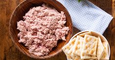 a wooden bowl filled with meat and crackers on top of a table next to a napkin