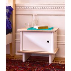 a small white cabinet sitting on top of a red rug next to a wooden shelf