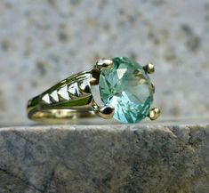 This beautiful and elegant sea foam green spinel ring holds true to the timeless designs of the late 1960's Mid-century period. The lines are strong and romantic, with just the right curves and flash to catch your eye. A 10 karat gold setting accentuates a large, light green synthetic spinel solitaire. Shifts and changes to the light and color give this ring a rich organic feel with layers of brightness and sparkle. Such an outstanding piece for any green stone lover! The stone measures 9mm and has great flashes of teal, mint and aqua. The rise off the finger measures 6.6mm. This beautiful piece has been well cared for and shows no large chips to the center stone. The inside of the band is no longer stamped but tests as 10 karat gold. The band has a nice thickness and the stone is secure i Classic Green Topaz Ring Gift, Classic Green Topaz Ring For Gift, Green Art Deco Ring With Round Cut, Heirloom Green Emerald Solitaire Ring, Green Round Cut Art Deco Ring, Vintage Emerald Ring For Promise, Art Deco Green Emerald Ring With Diamond Cut, Vintage Emerald Ring With Center Stone, Art Deco Round Green Emerald Ring