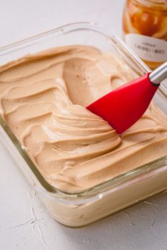 a red spatula scooping peanut butter out of a glass dish on a table